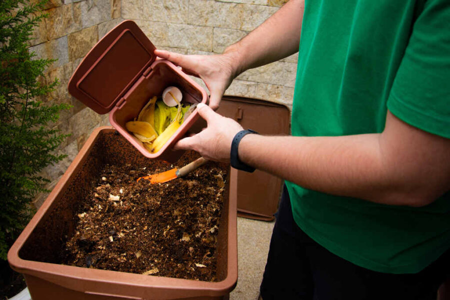 Homem colocando restos de frutas e vegetais para compostagem na composteira, para servir como adubo organico para as plantas do jardim